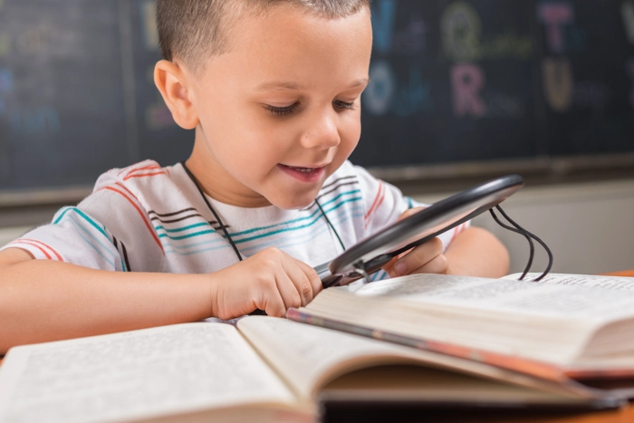 young boy using magnifying glass to read a book