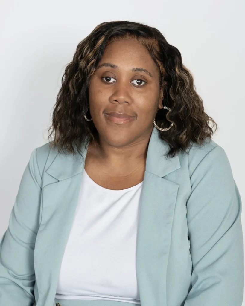 Head-and-shoulders portrait of a woman with wavy hair wearing a light blue blazer and white top, against a neutral gray background.