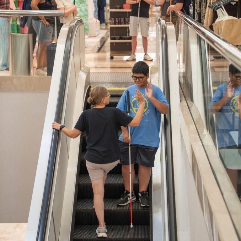 Image of visually impaired teenage boy going down escalator with instructor
