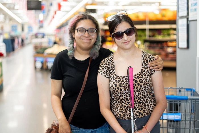 Two College Prep Program students, one using a white cane, shopping together during a community outing.