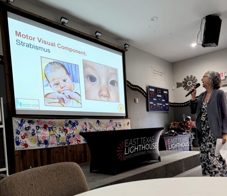 Woman speaker with microphone presenting a slide about strabismus, showing a baby and an eye image on the screen.